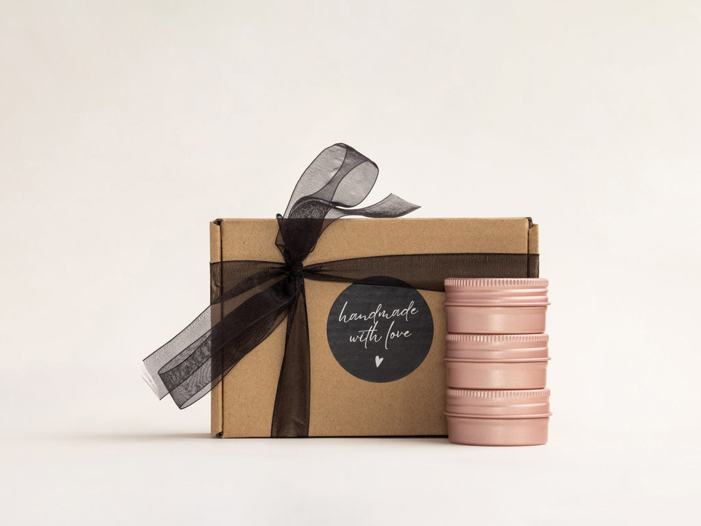 AKUN Essence of Life rose tin candles stacked beside a kraft gift box finished with a black ribbon and handmade label