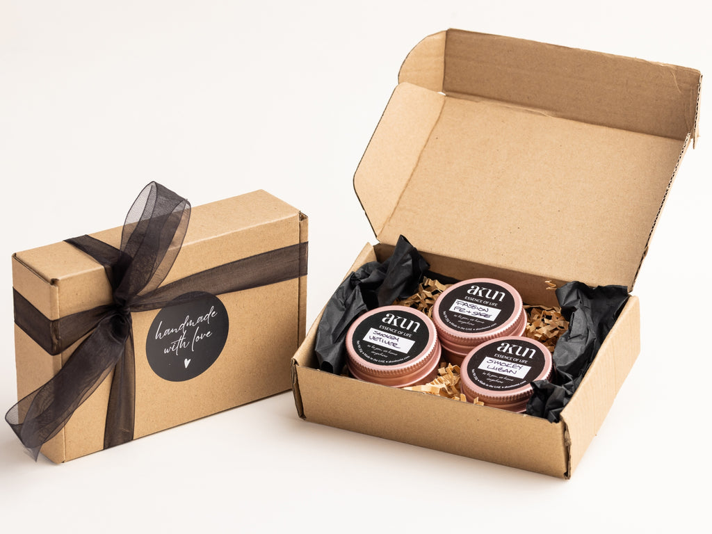 AKUN Essence of Life rose tin candles revealed inside an open kraft gift box, showcasing a curated trio of fragrances