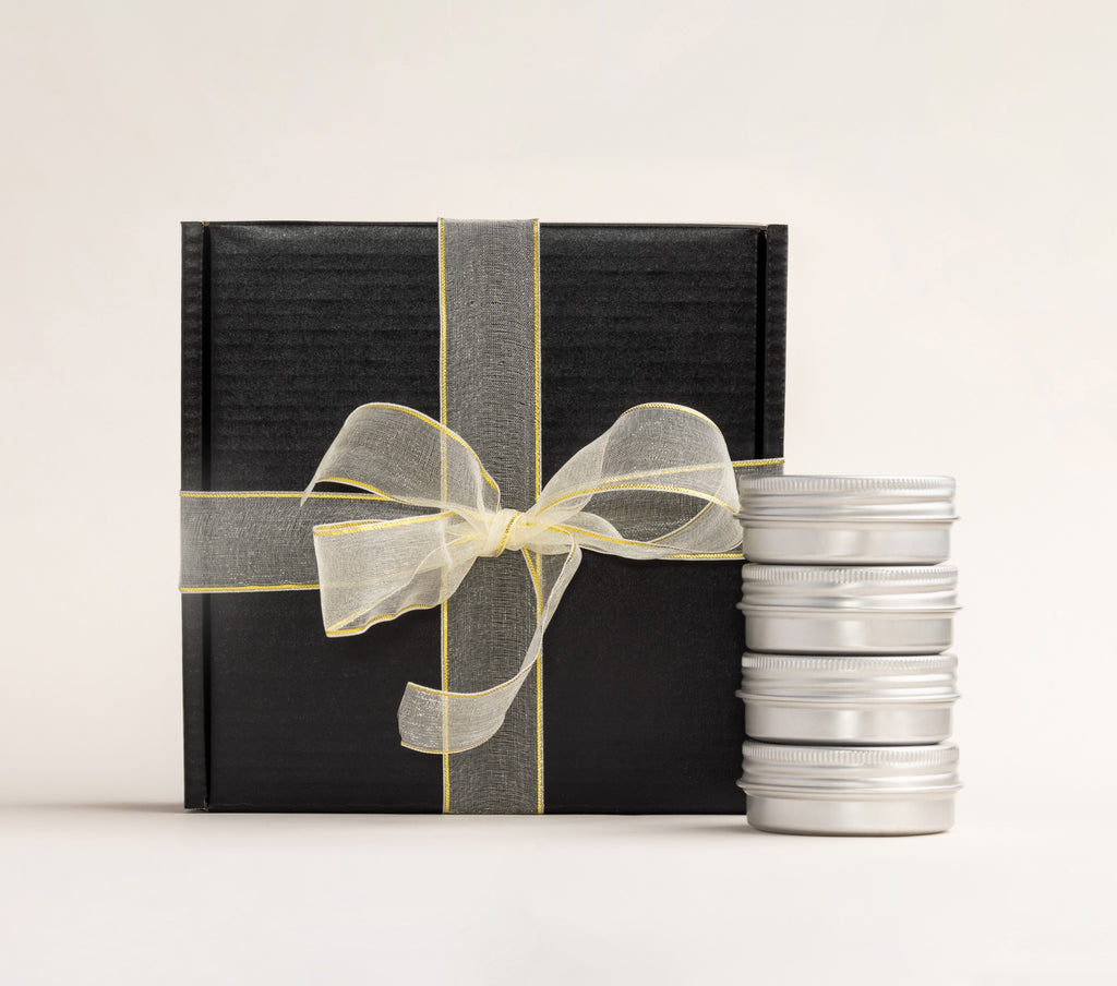 AKUN Scents of Arabia discovery candles arranged beside a ribbon-wrapped black box, highlighting the tin collection format